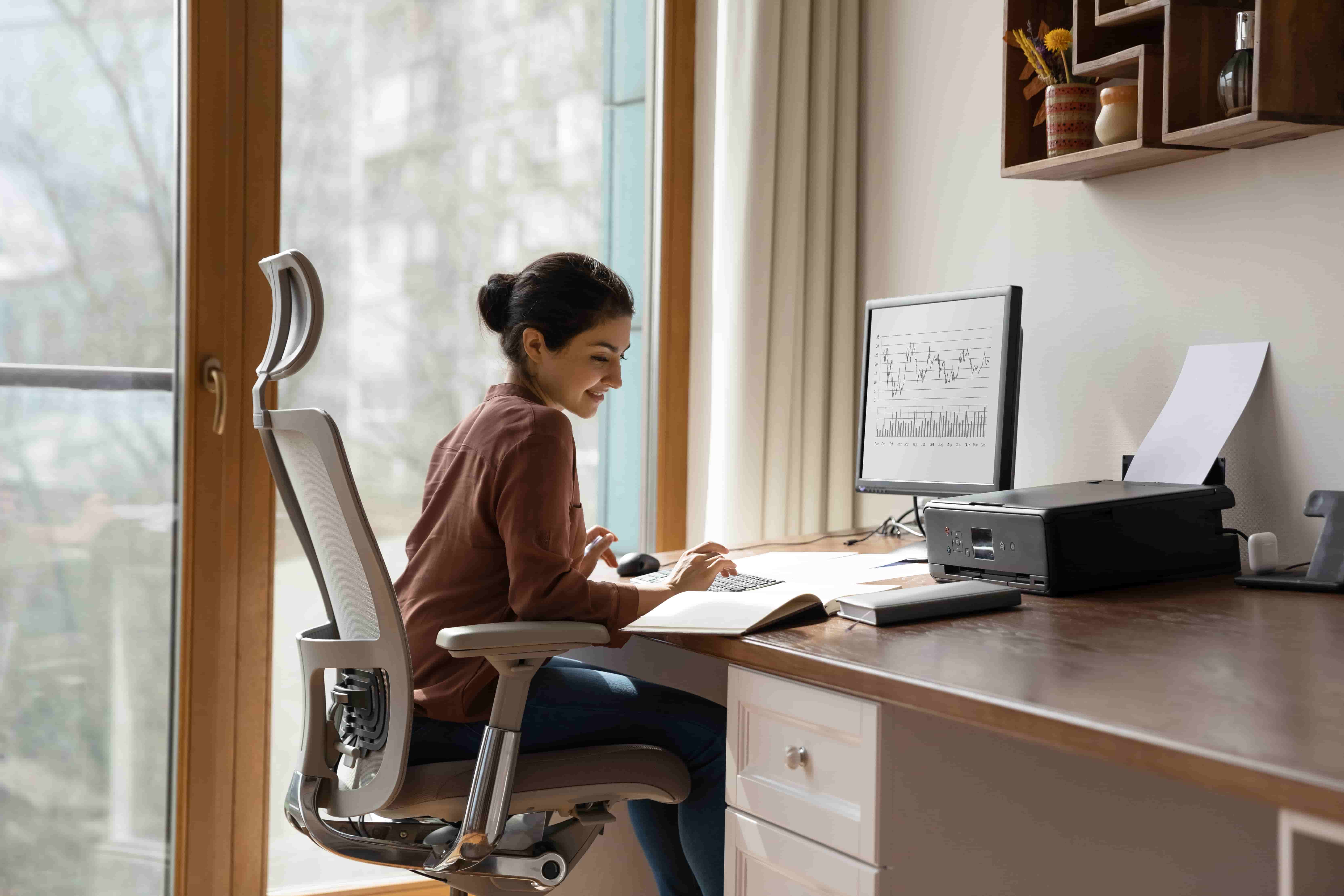 Concentrated young indian ethnicity woman sitting in comfortable adjustable ergonomic armchair with lumbar support, studying or working on computer in modern home office. distant workday concept.